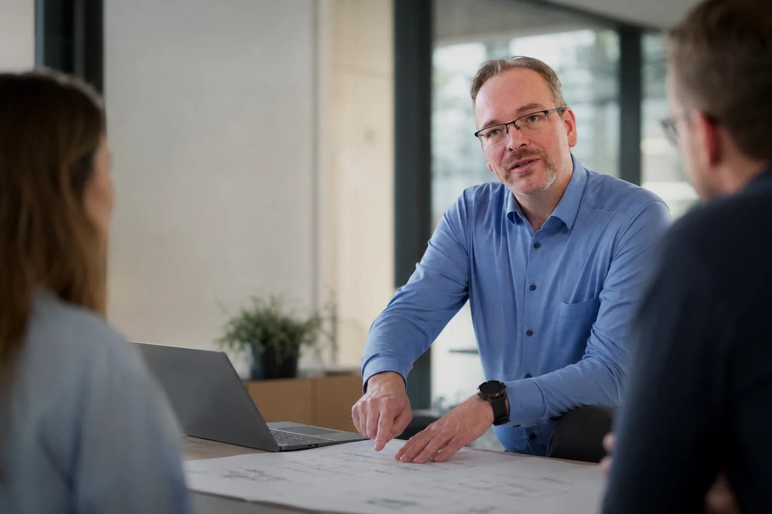 Christian Höhle bespricht mit zwei Mitarbeitenden einen konkreten Arbeitsprozess am Projekttisch